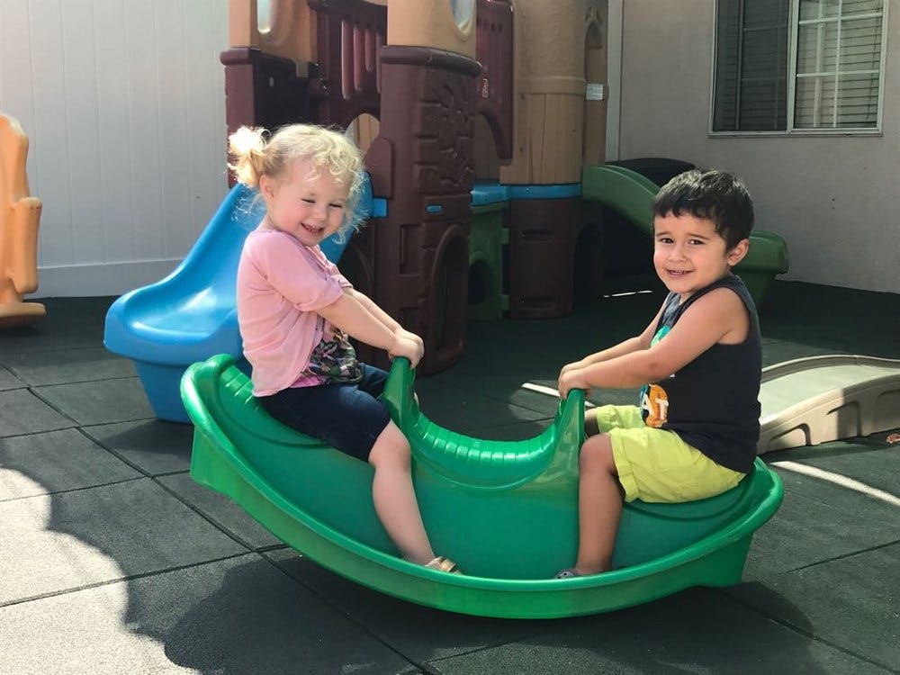 Two children on a green seesaw rocker on a playground