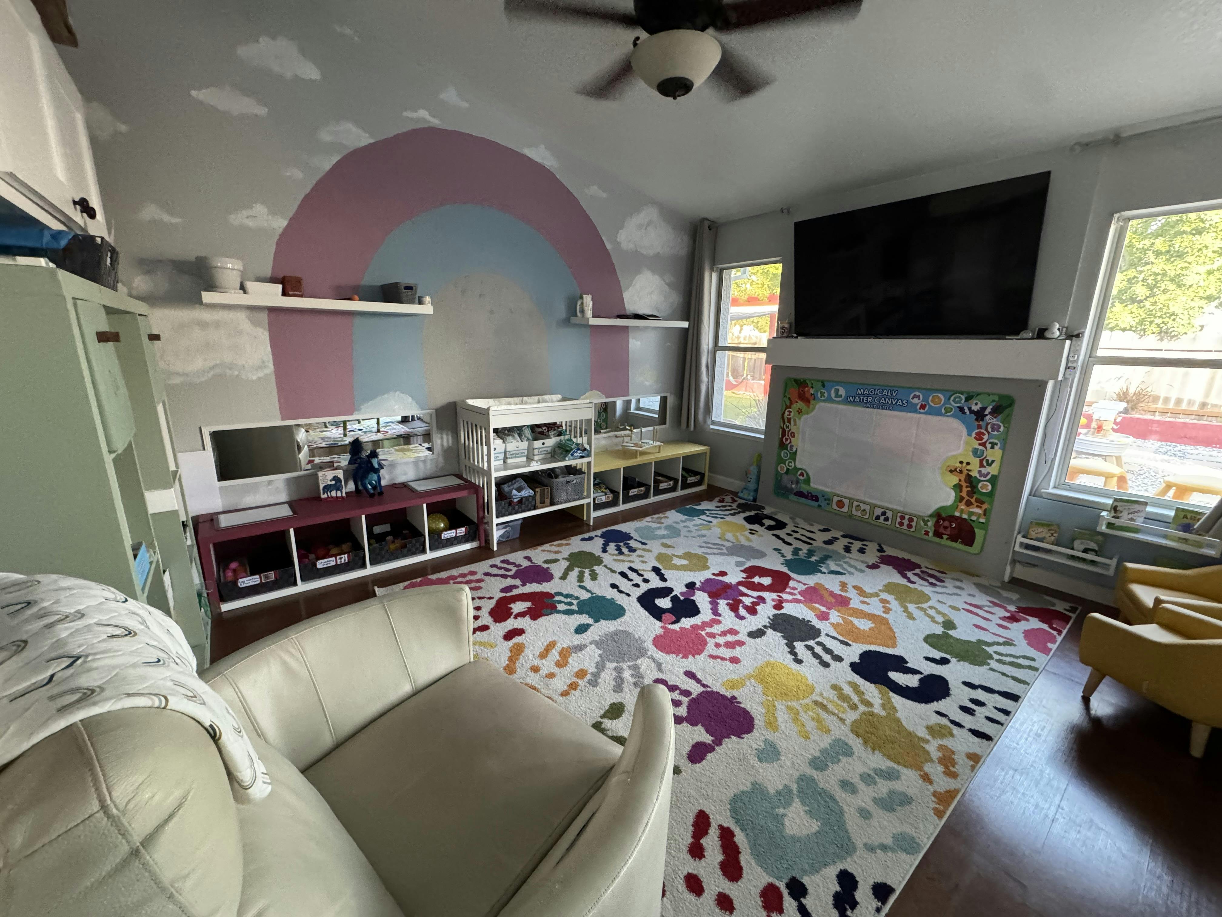 Playroom with a rainbow mural, handprint rug, and white furniture