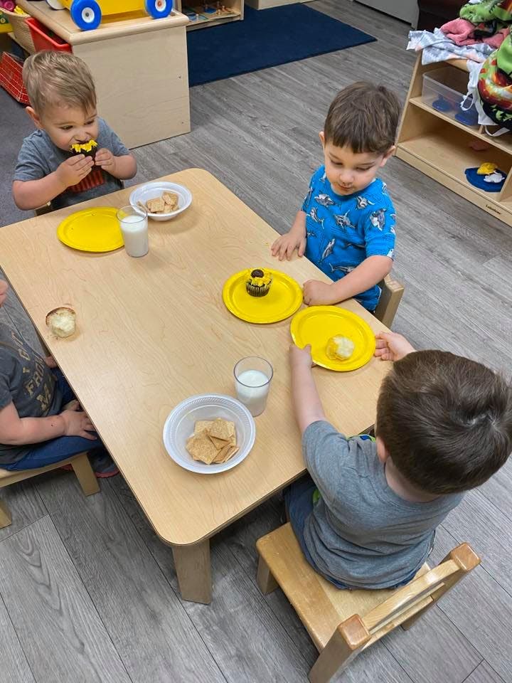 Three children sitting at a table with snacks and drinks