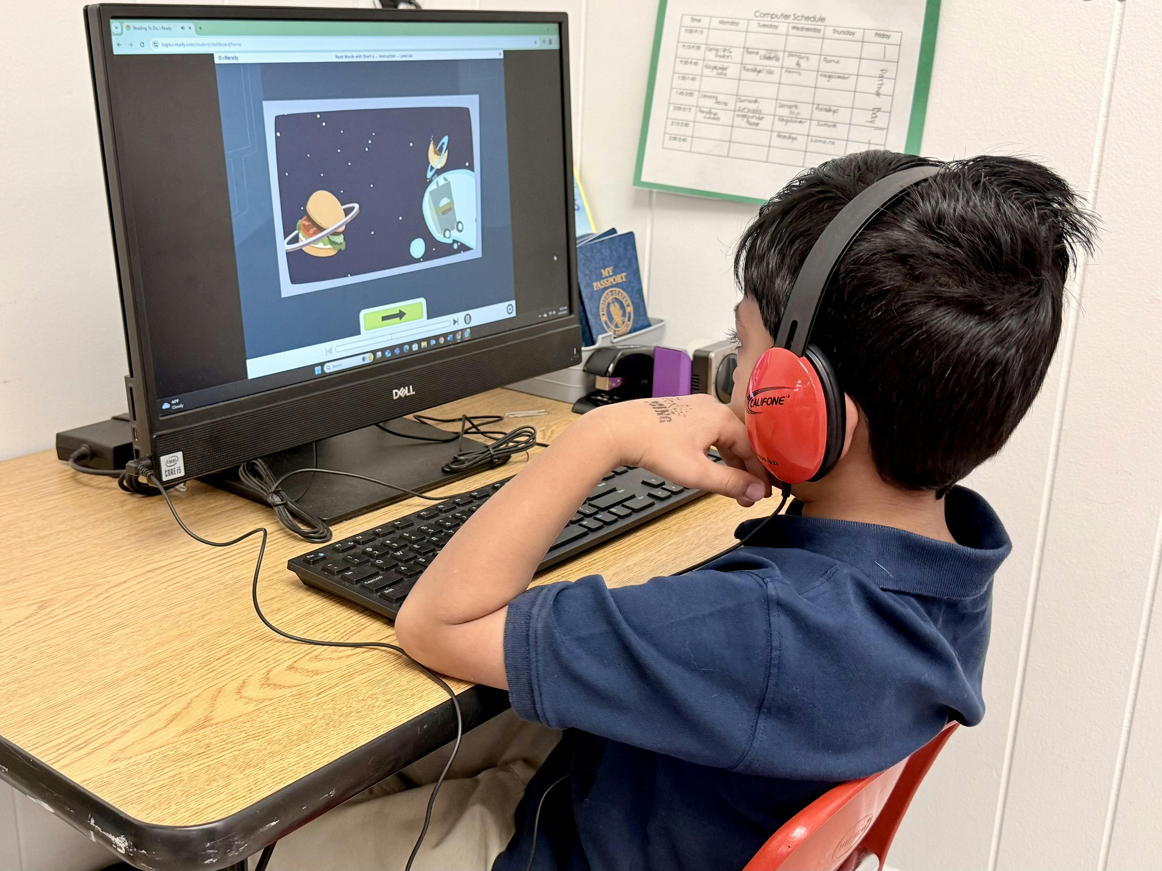 Child wearing red headphones, looking at a computer screen in a classroom