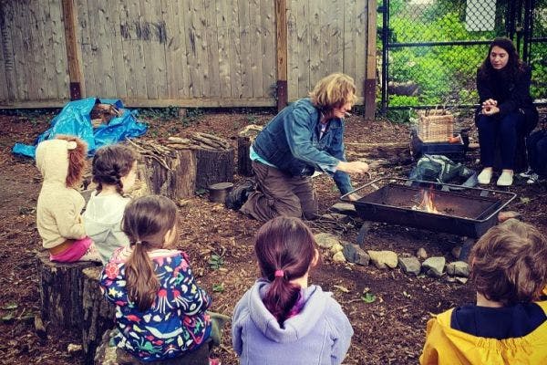 Person kneeling by a fire pit with children sitting around it