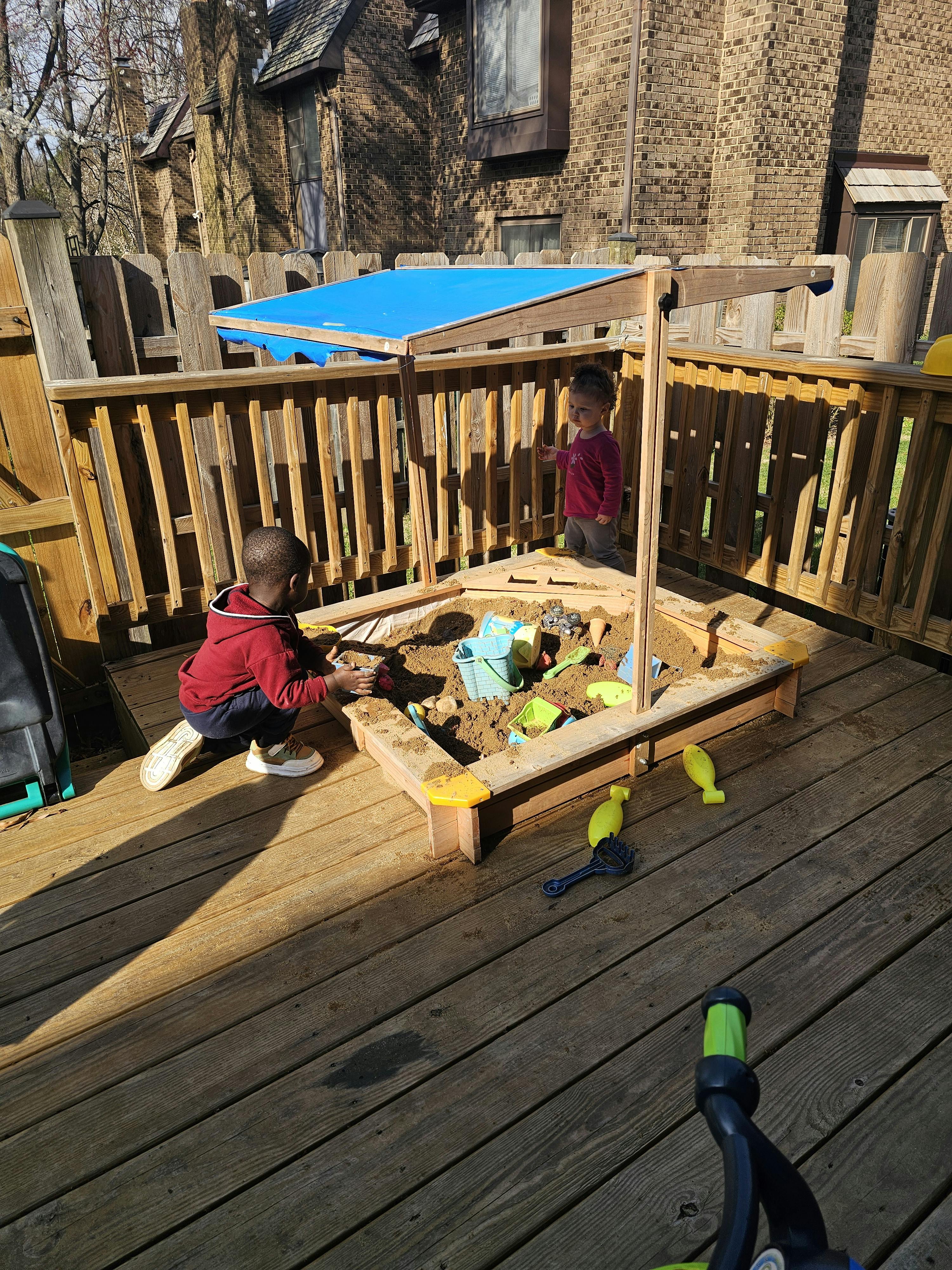 Two children playing in a wooden sandbox on a deck