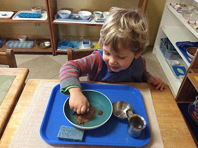 Child playing with items in a bowl on a tray