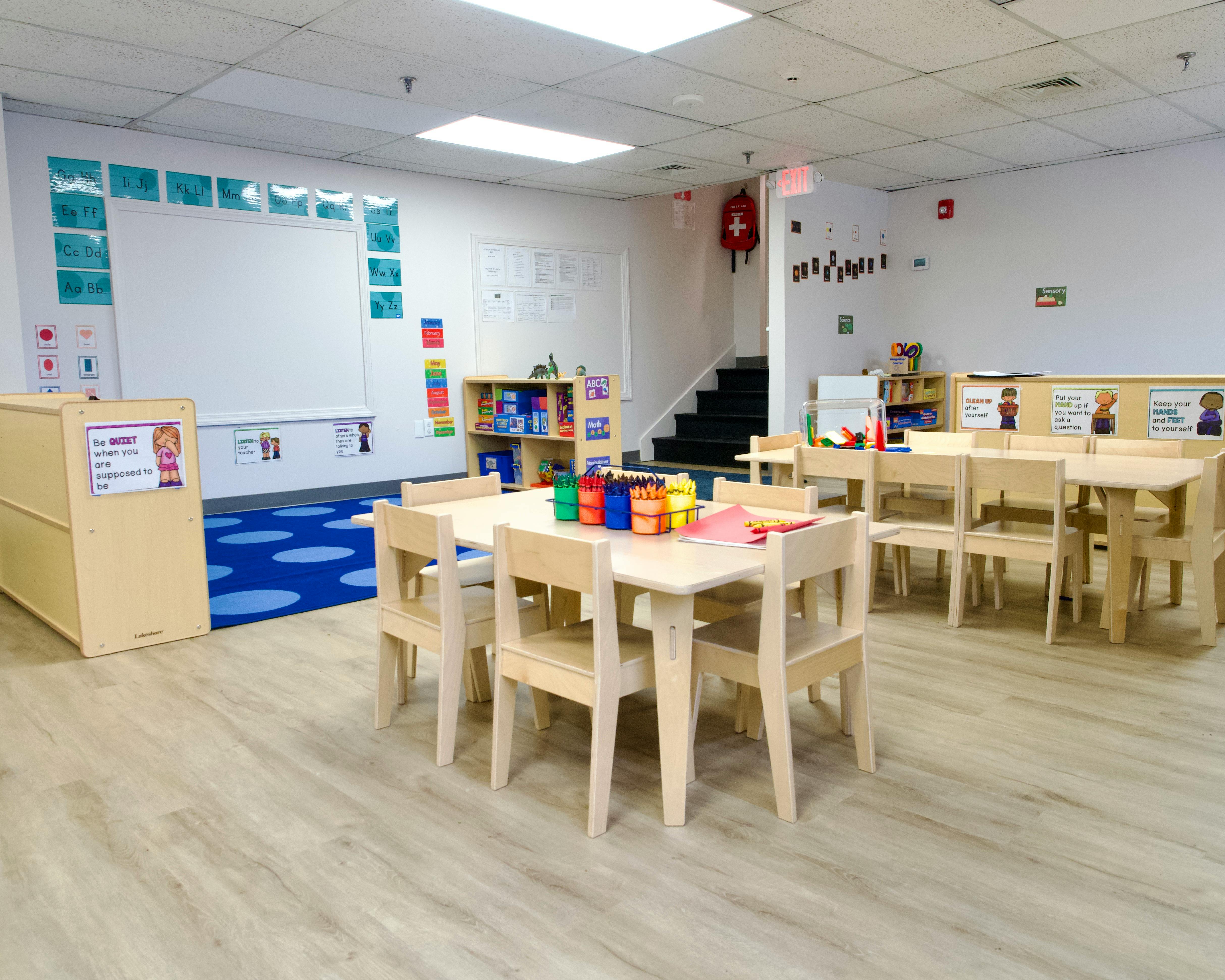 Classroom with small tables and chairs, whiteboard, and blue rug