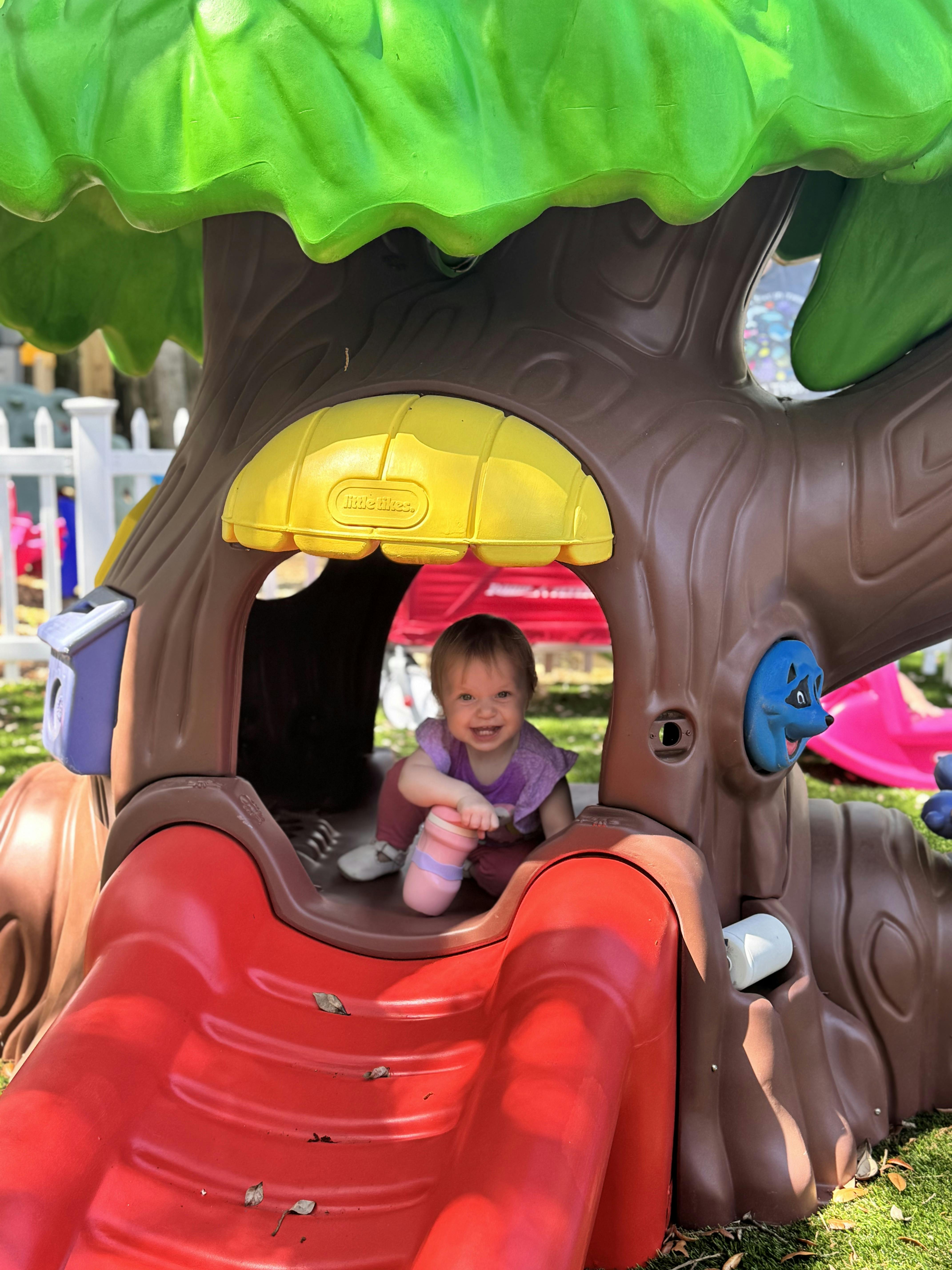 Child sitting in a play structure shaped like a tree