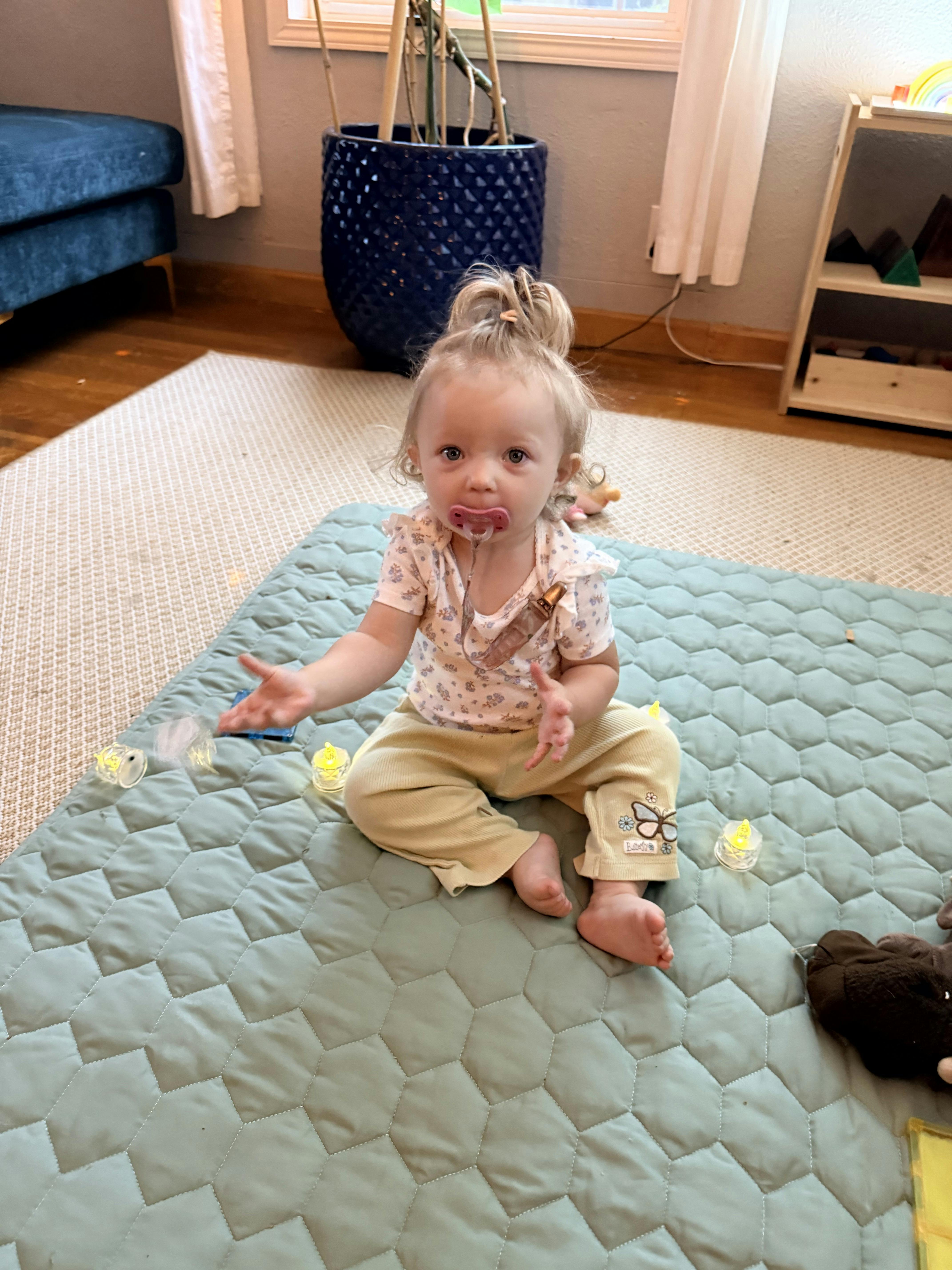A toddler sitting on a quilted floor mat with small LED lights