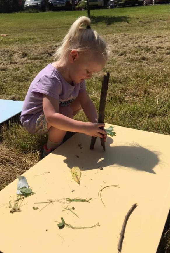 Child playing with sticks and leaves on a board outdoors