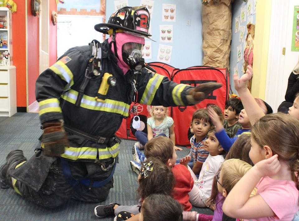 Person in firefighter gear kneeling and gesturing to a group of children