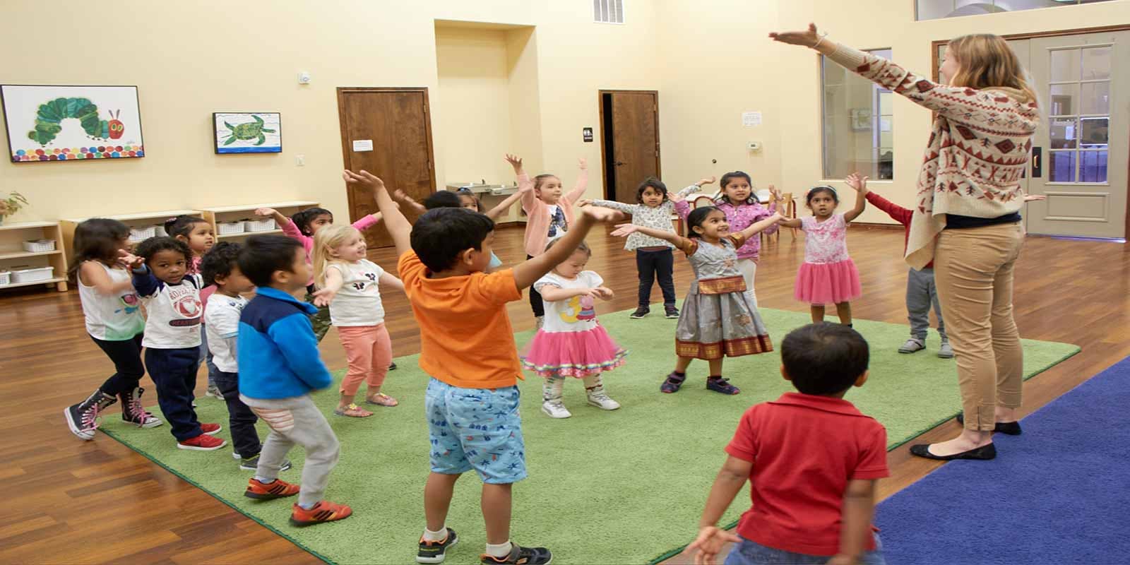 Adult leading a group of children in an activity with arms raised