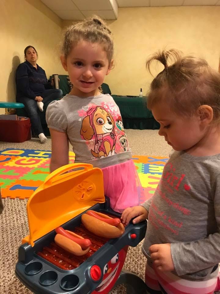 Two children playing with a toy grill with hot dogs