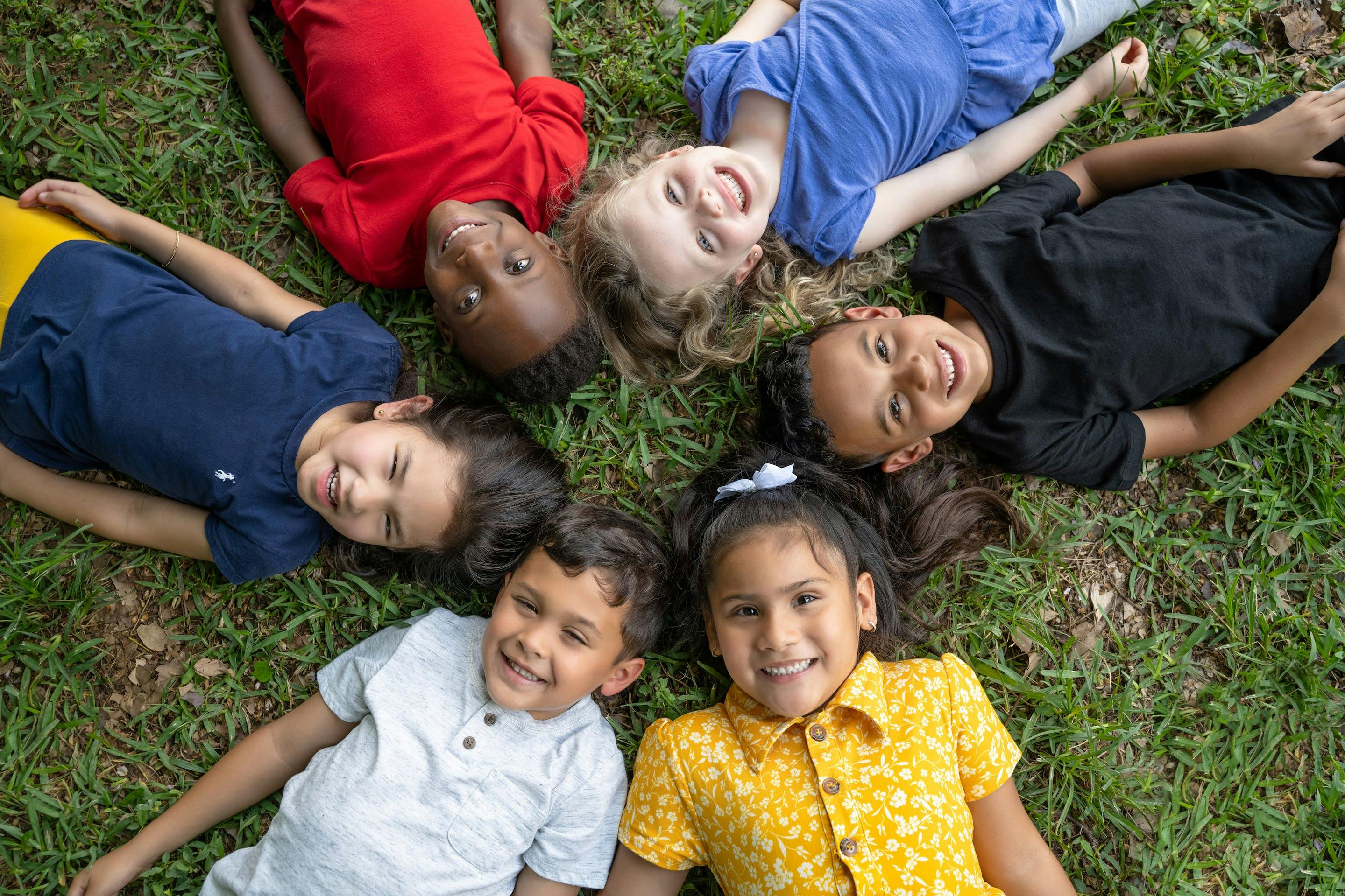 Six children lying in a circle on grass, looking up