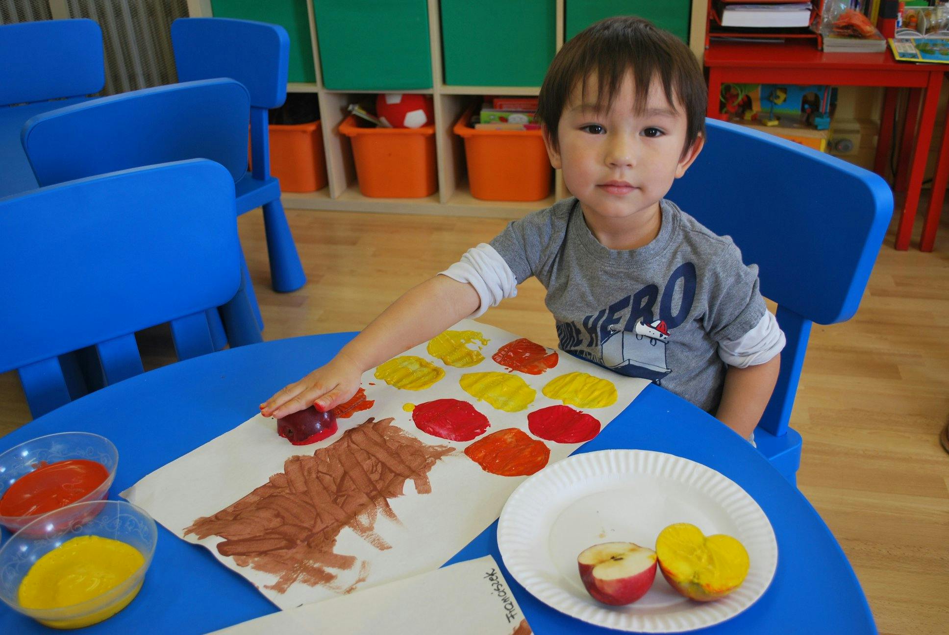 Child at a table doing an art activity with paint and apple halves