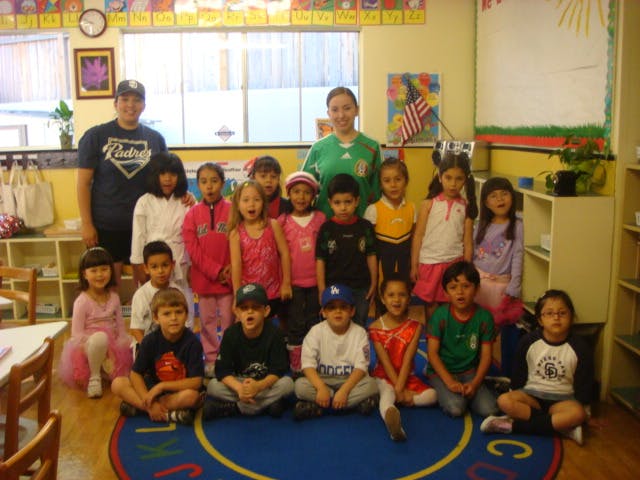 Two adults and a group of children posing in a classroom