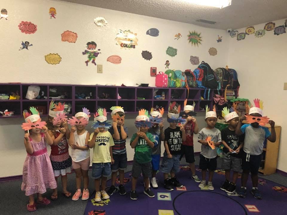 Children in a classroom wearing paper hats and feather hats