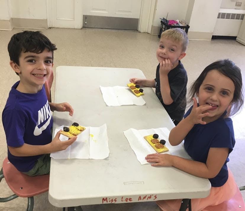 Three children sitting at a table with snacks