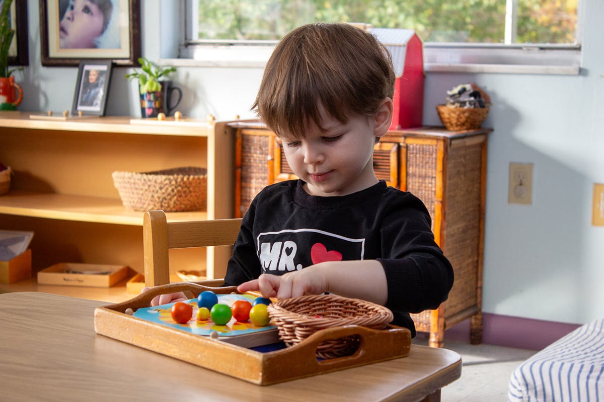 Child playing with colorful pegs and a basket on a wooden tray