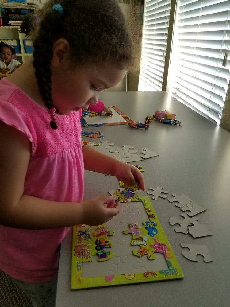 Child in pink shirt assembling a puzzle on a table