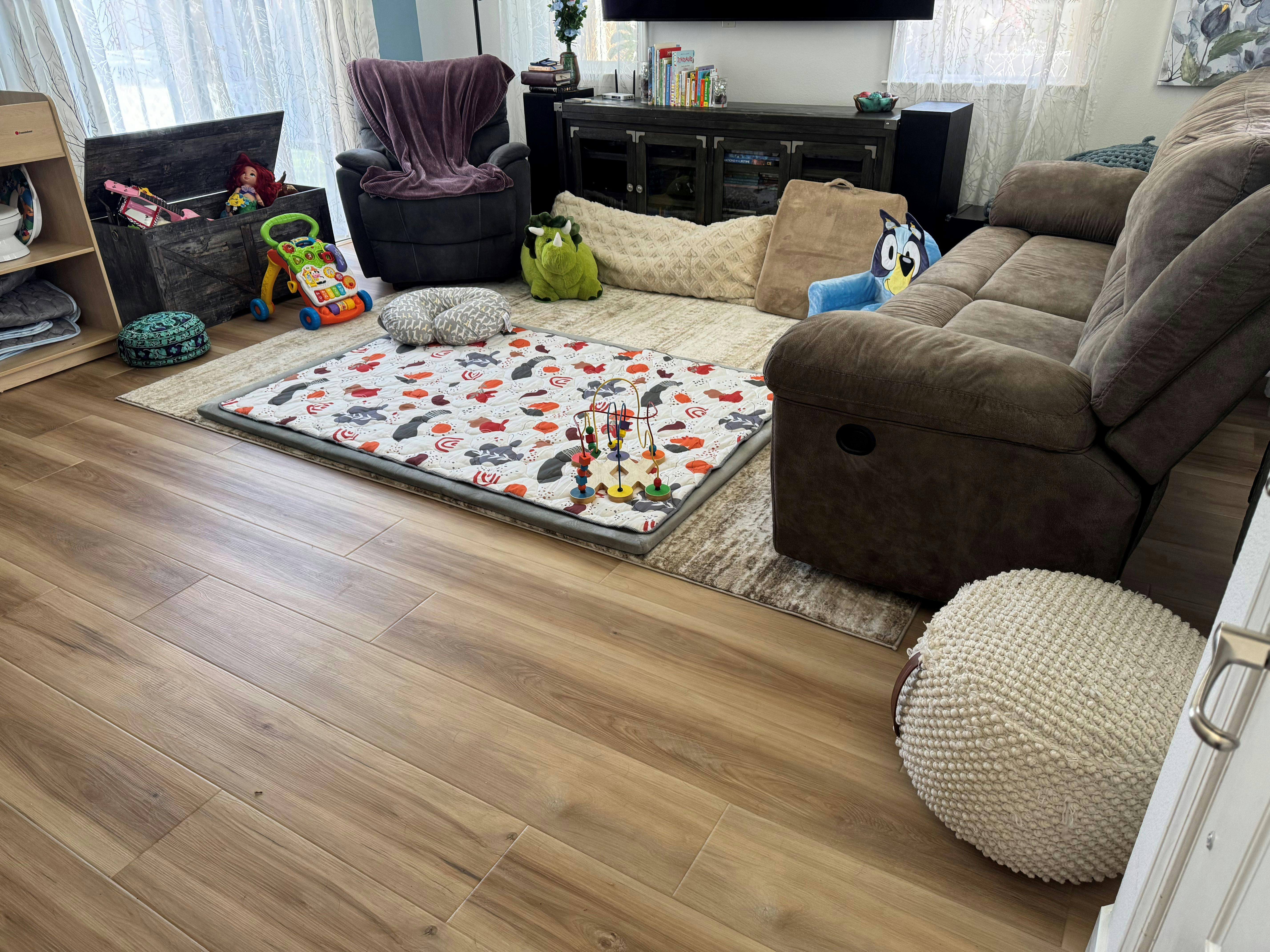 Living room with wood floor, a play mat with toys, and furniture