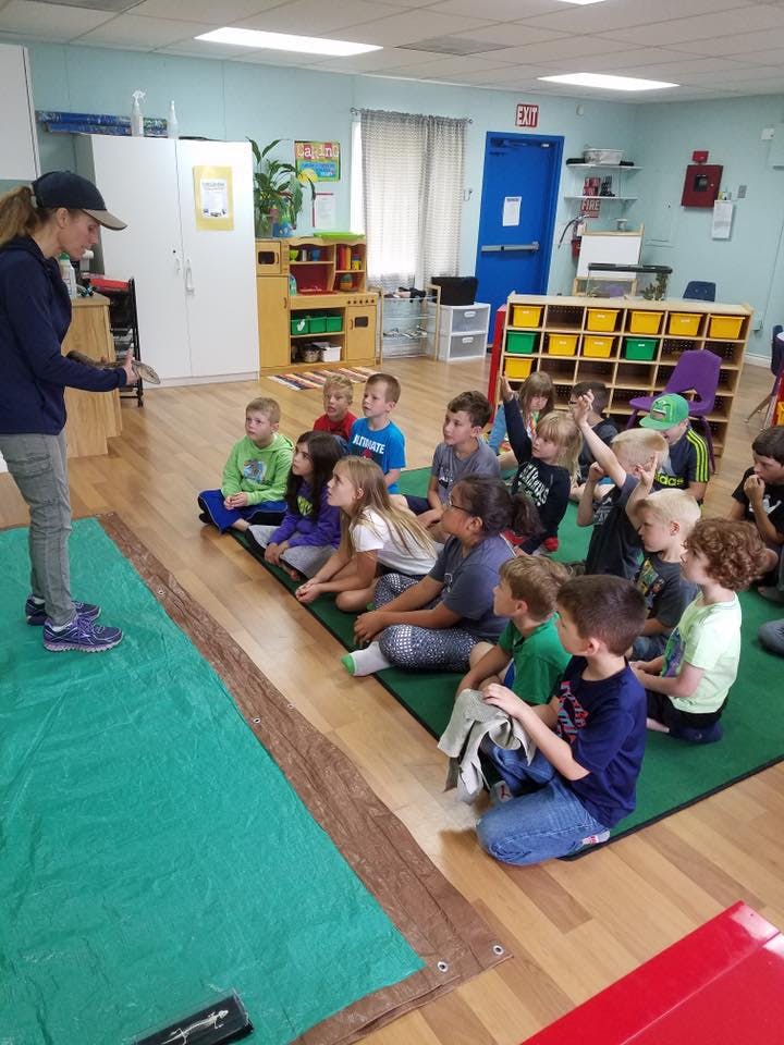 Adult speaking to a group of children sitting on the floor in a classroom