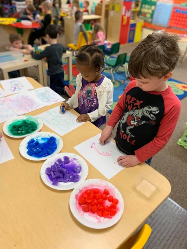 Two children drawing at a table with colorful paints in plates