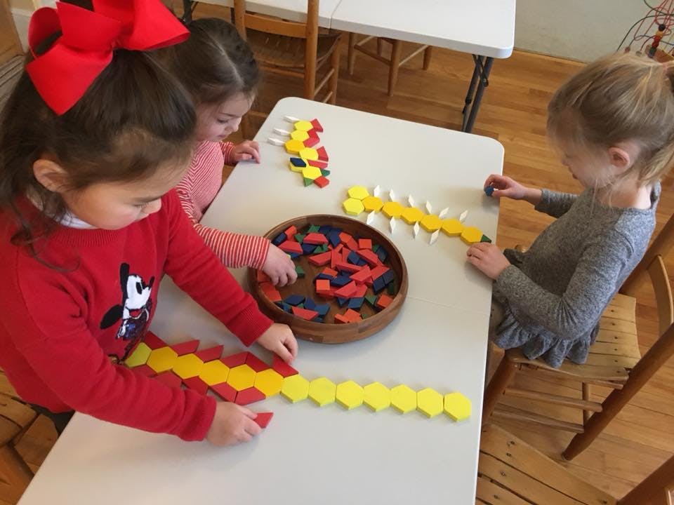 Three children playing with colorful geometric shapes at a table