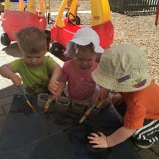 Three children painting on a dark surface outdoors