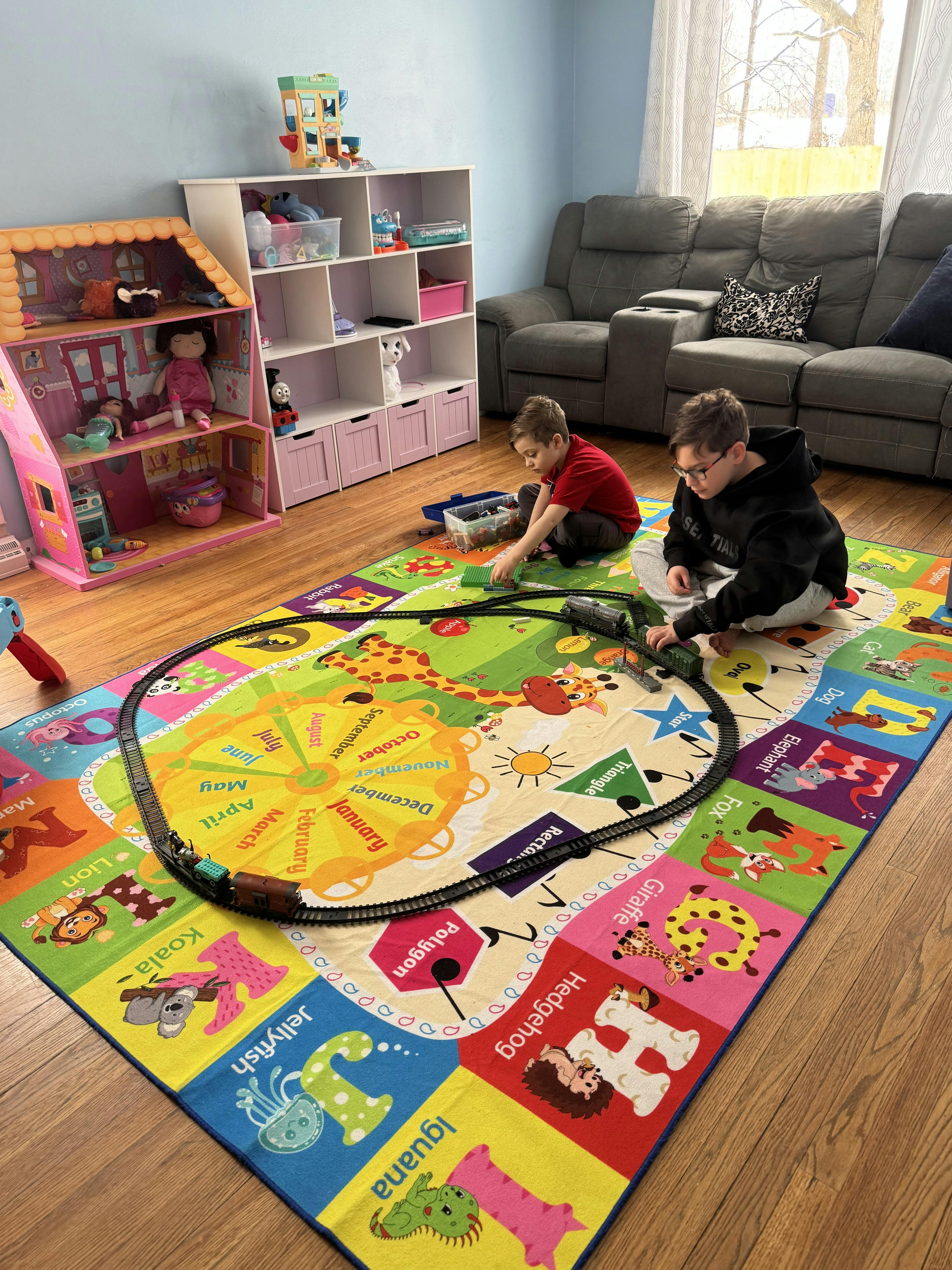 Two children playing with a toy train set on a colorful alphabet rug