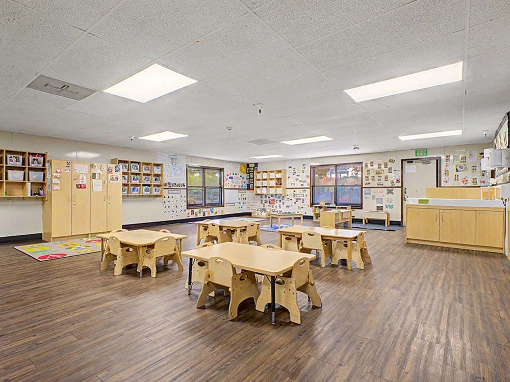 Classroom with small wooden tables and chairs, shelves, and decorated walls