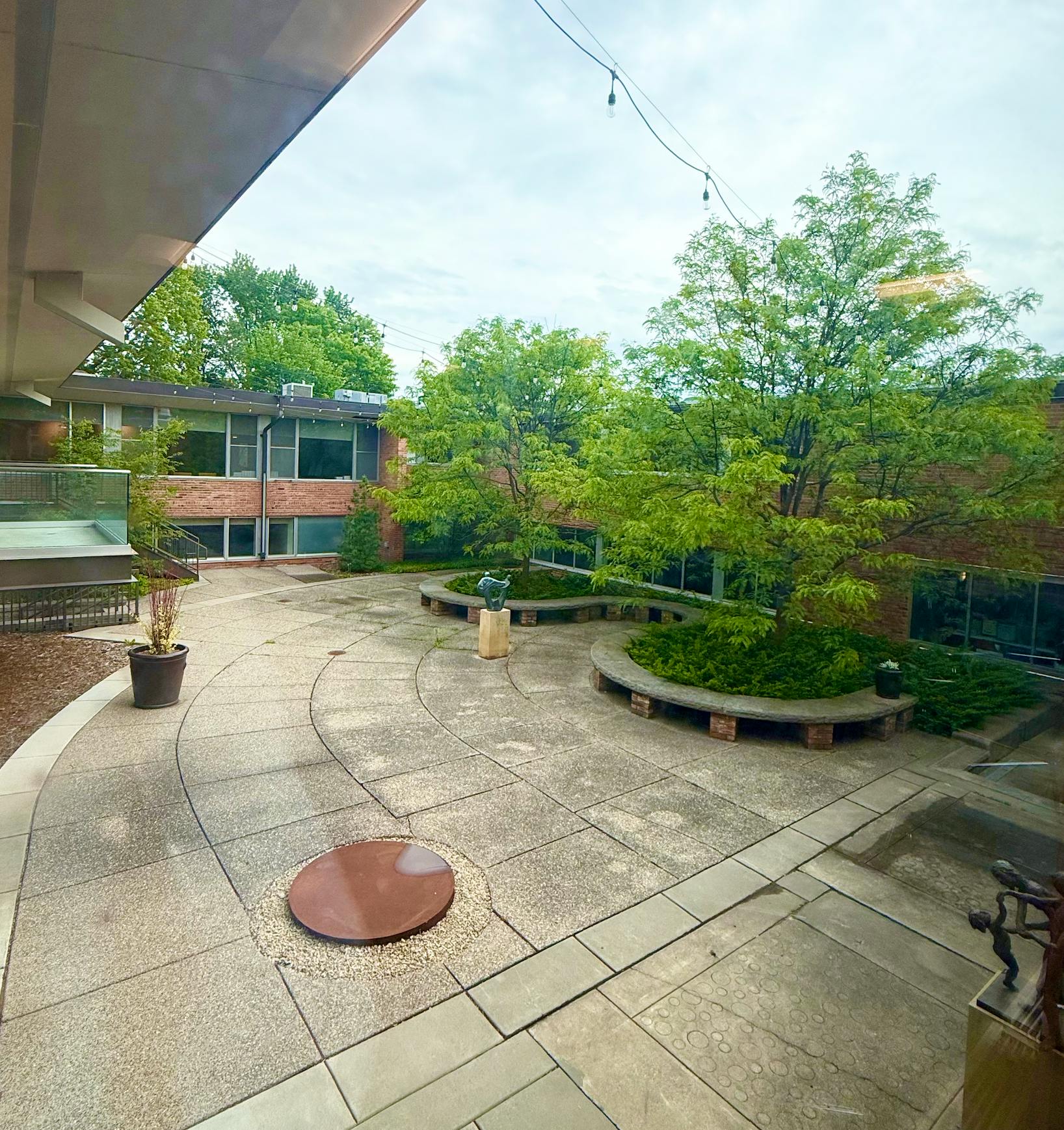 An outdoor courtyard with trees, a brick building, and a circular stone patio