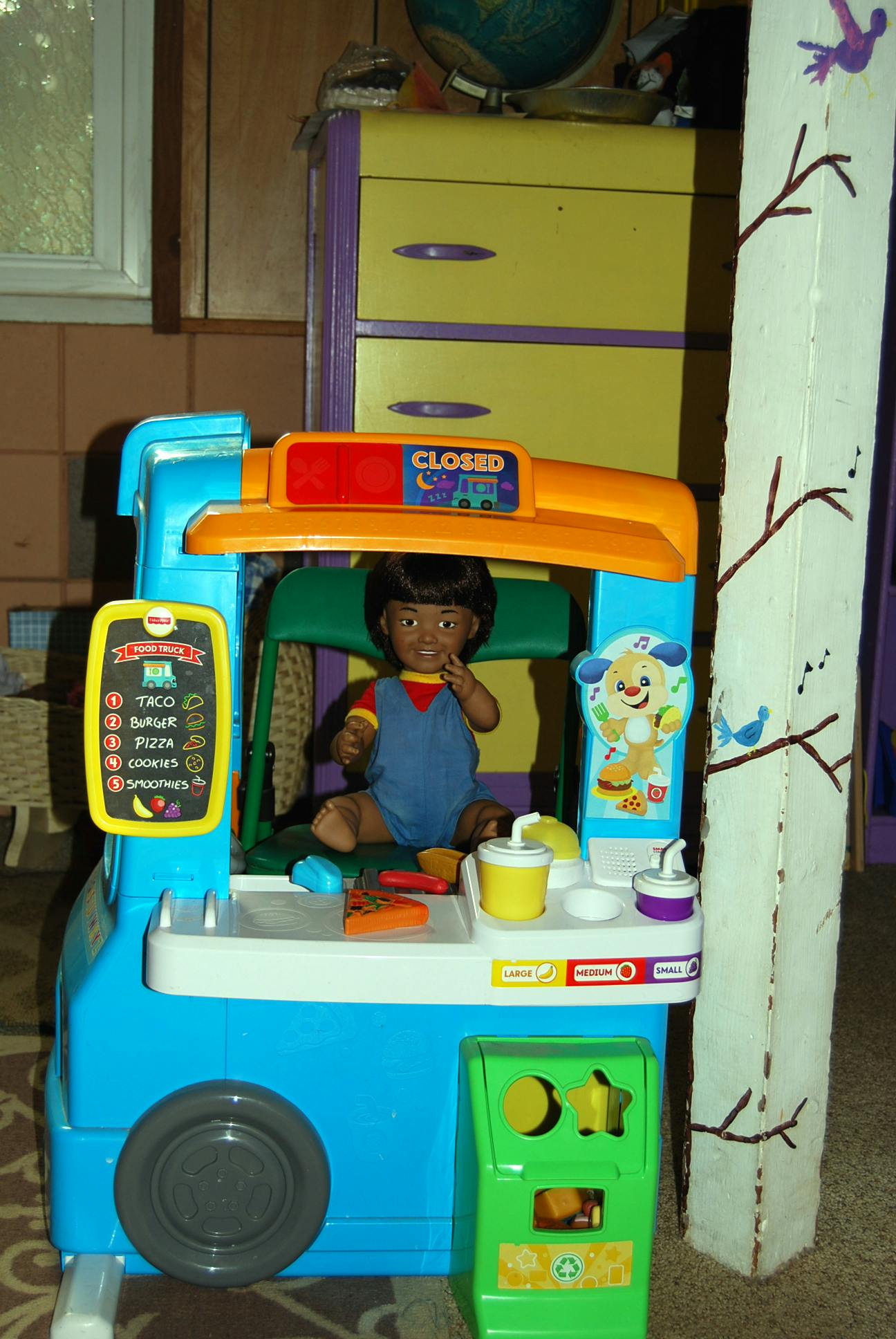 Doll sitting in a toy food truck with a menu board and play food