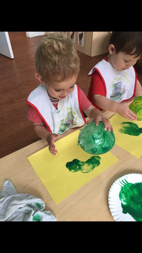 Two children painting with green paint and balloons