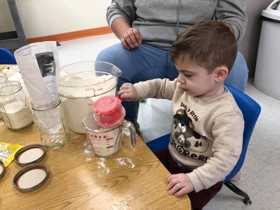 Child pouring from a red scoop into a measuring cup