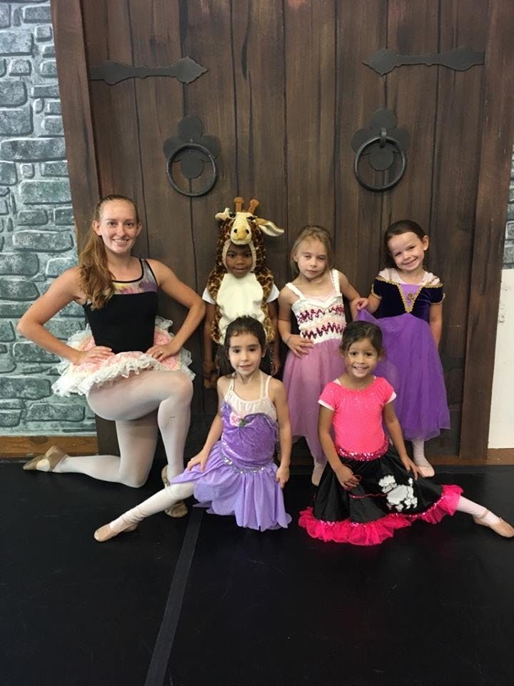 Person in ballet attire kneeling with children in costumes