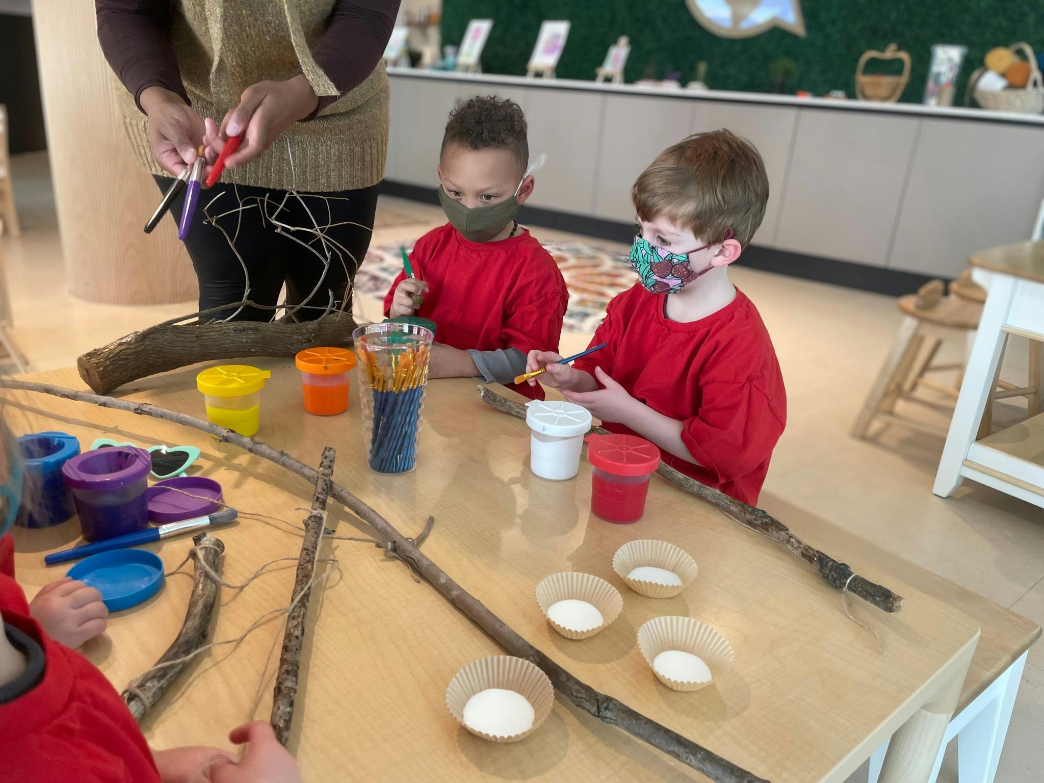 Person and two children at a table with craft supplies and sticks