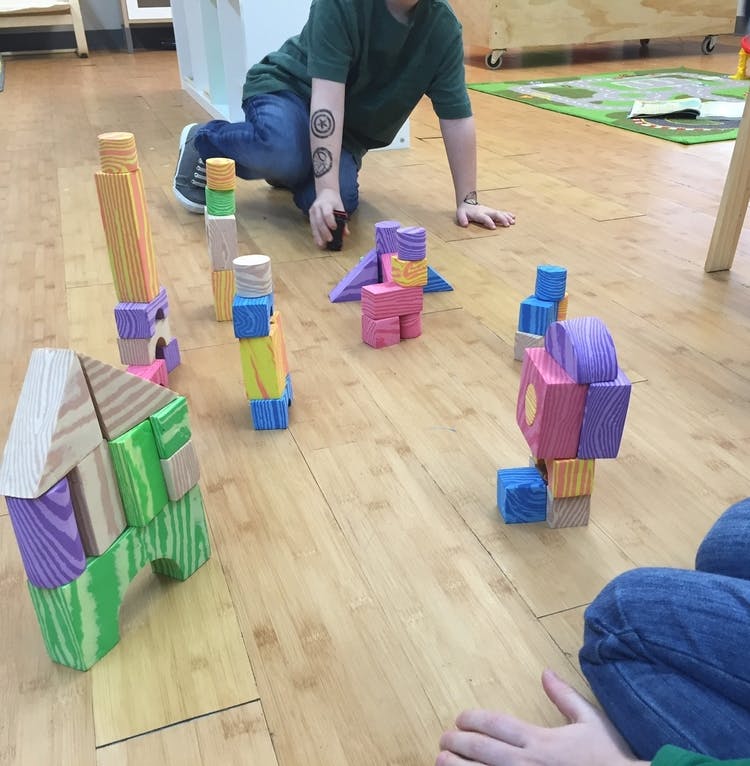 Person on knees playing with colorful building blocks on a wooden floor