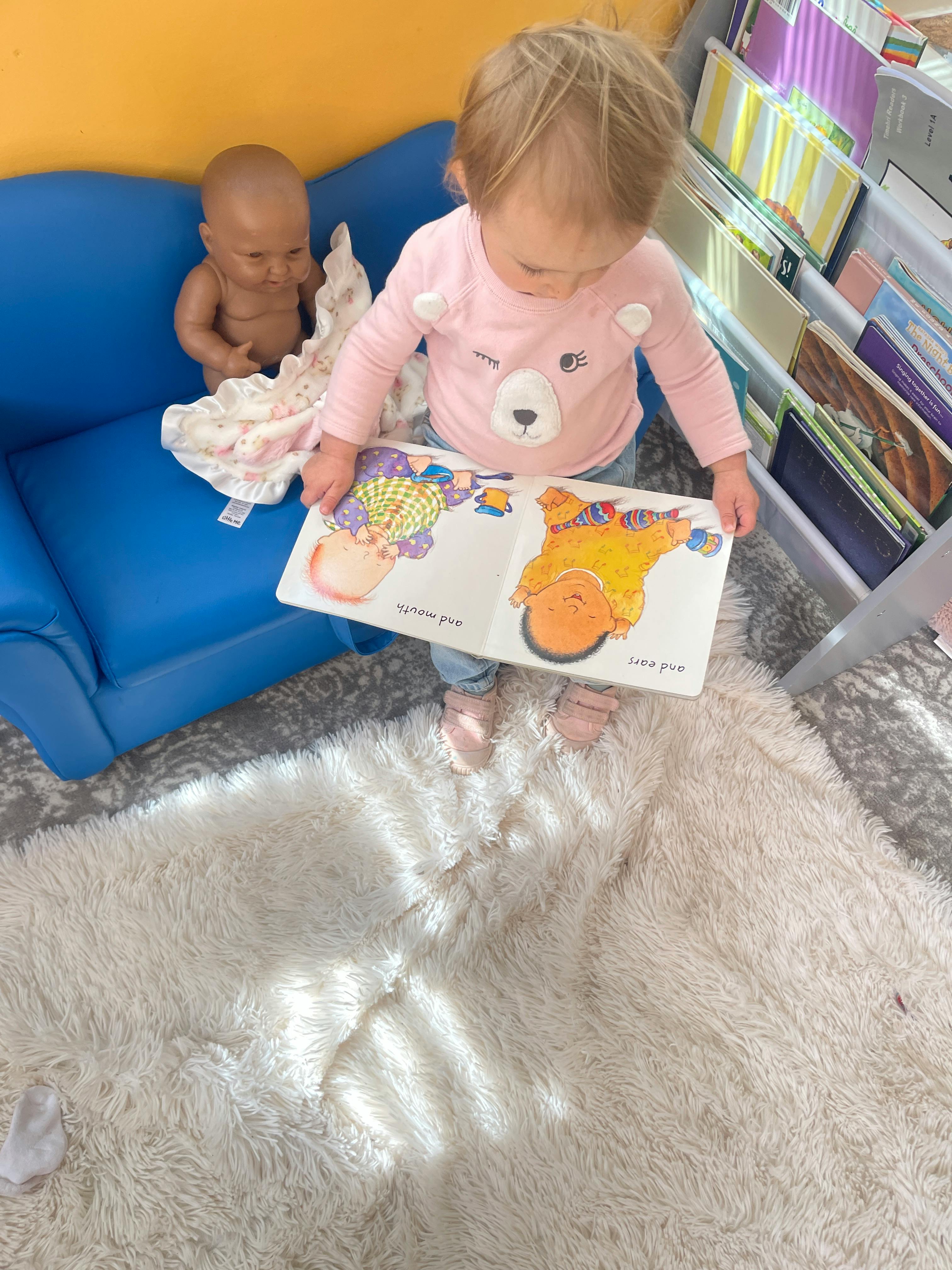 Child standing on a rug holding an open book with illustrations