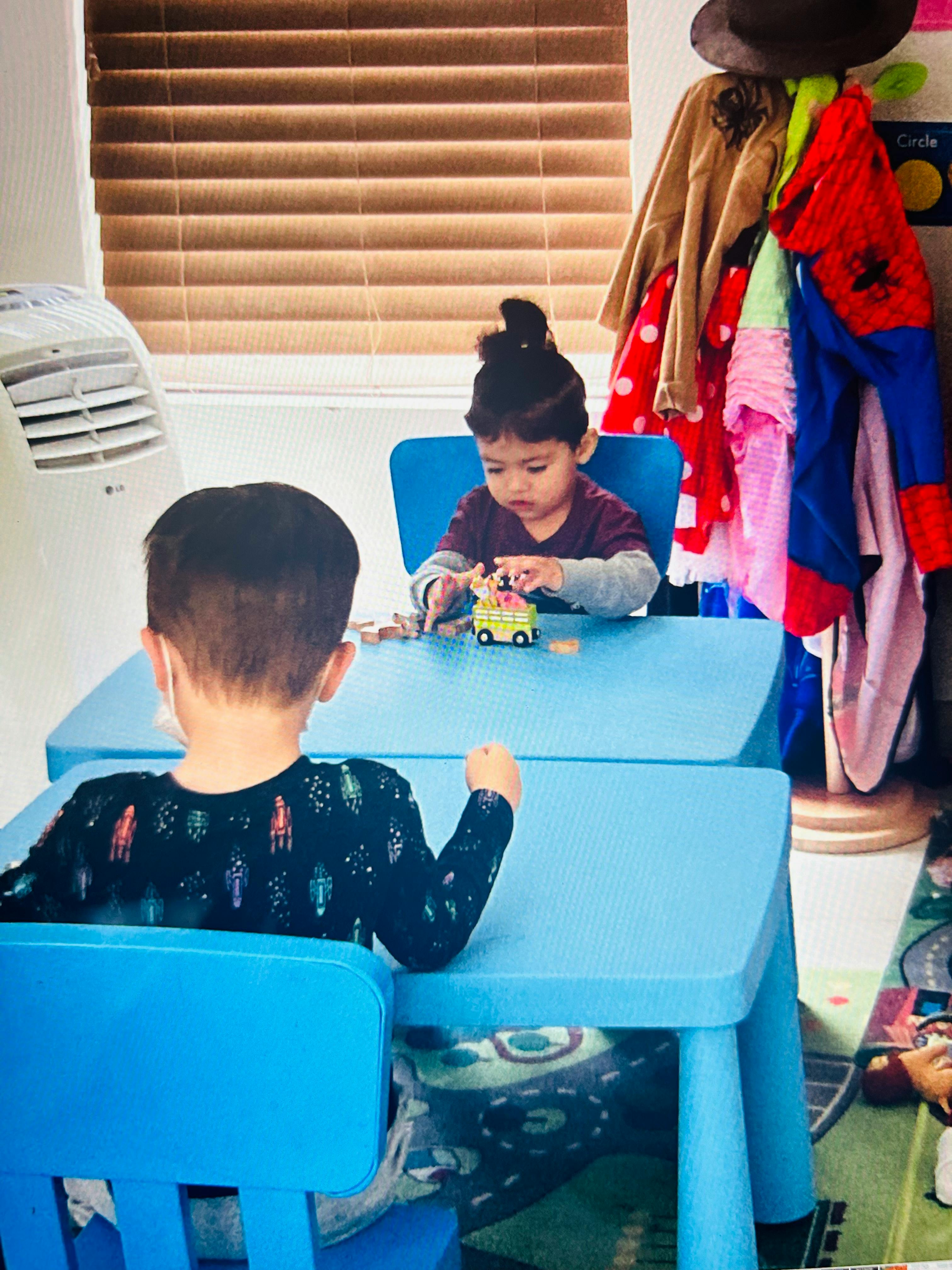 Two children sitting at blue tables, one playing with a toy car