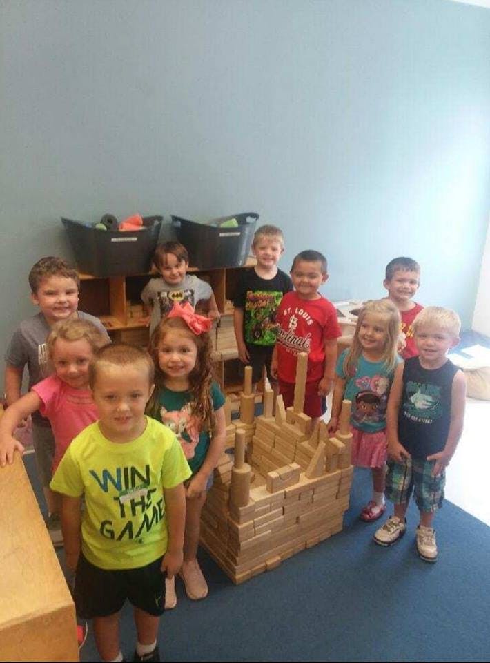 Group of children standing around a large wooden block structure in a classroom