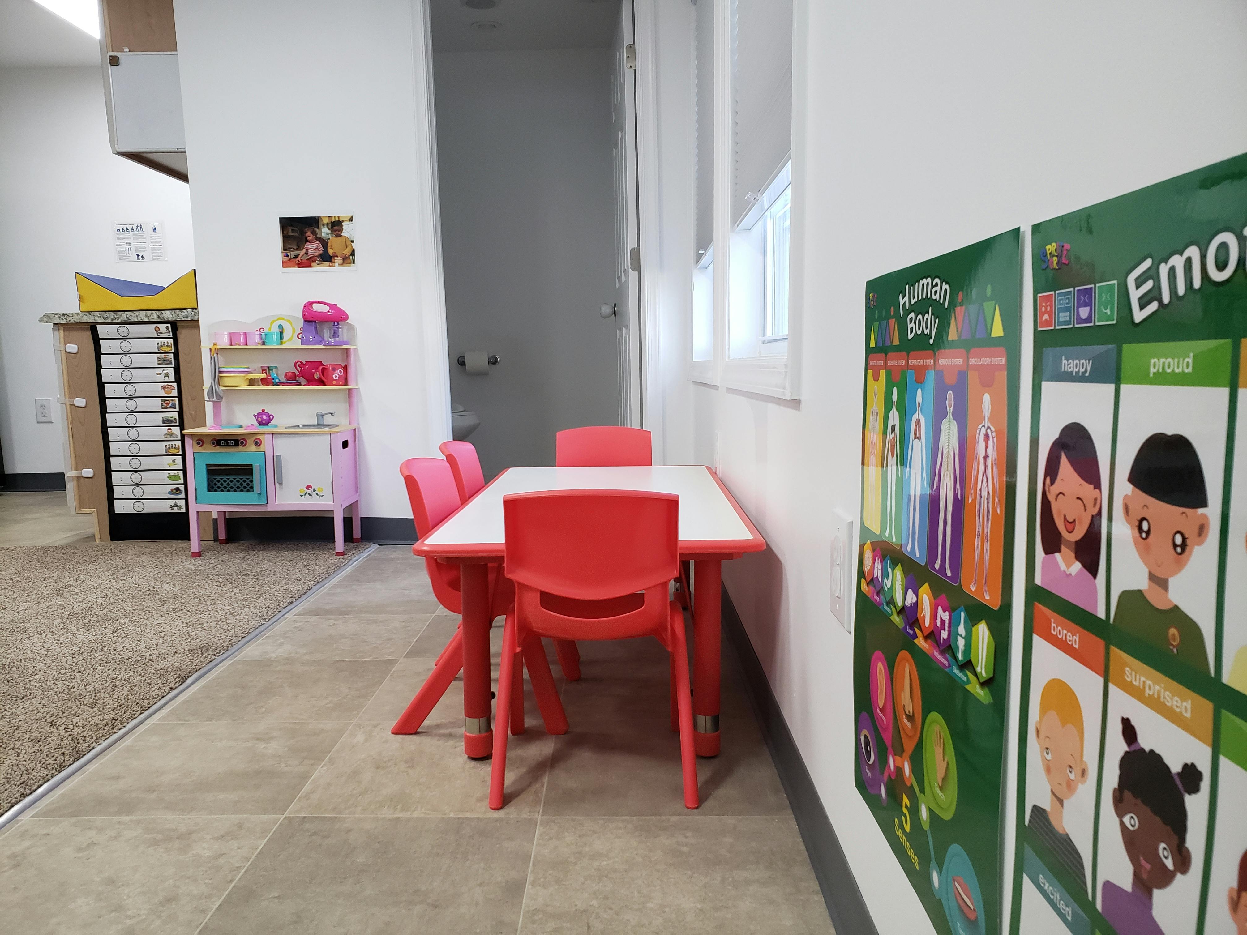 Children's play area with small red table and chairs, toy kitchen, and posters