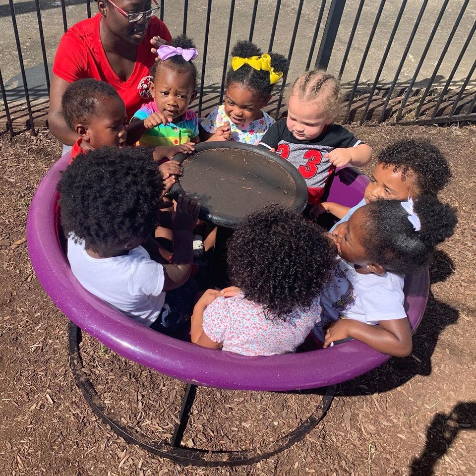 Person and multiple children gathered around a table on a playground