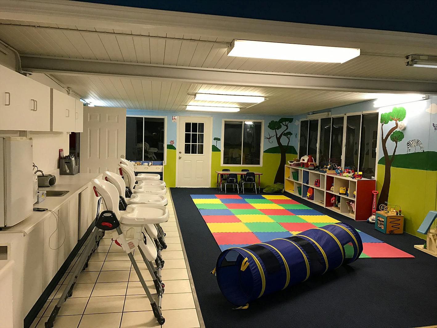 Playroom with colorful floor mat, play tunnel, and high chairs