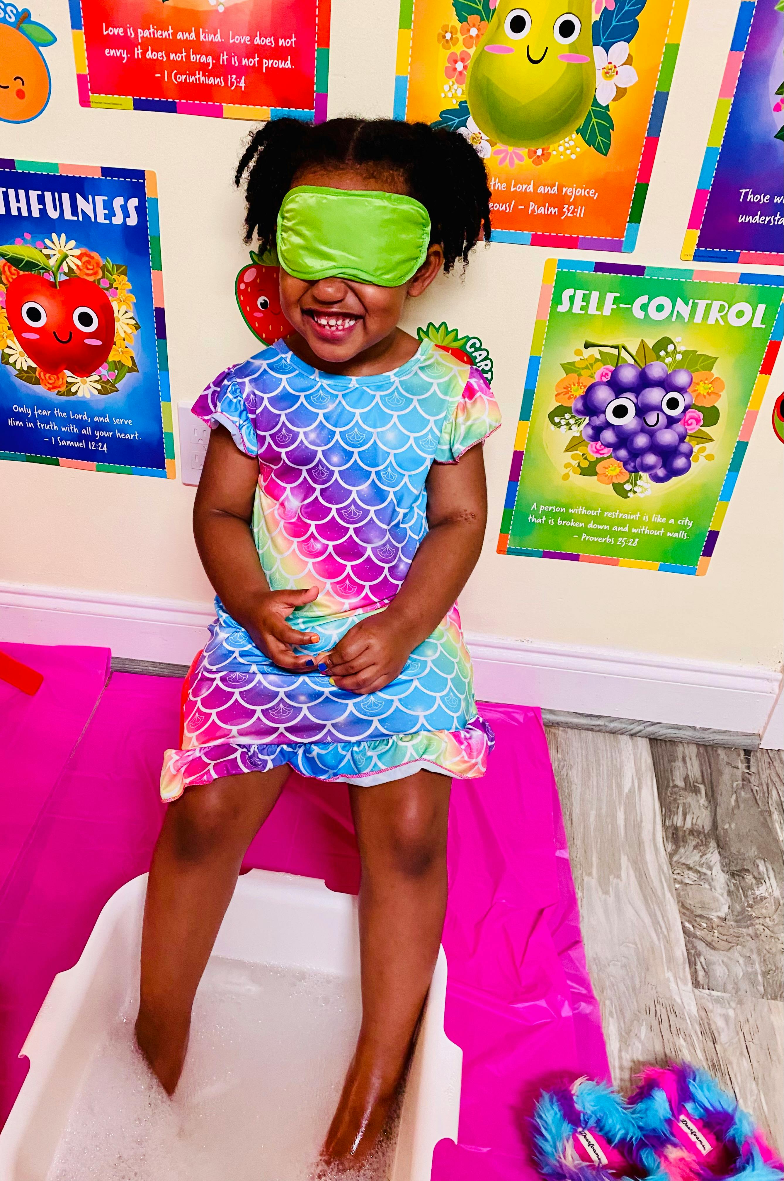 Child with an eye mask on their face, feet in a bubble bath