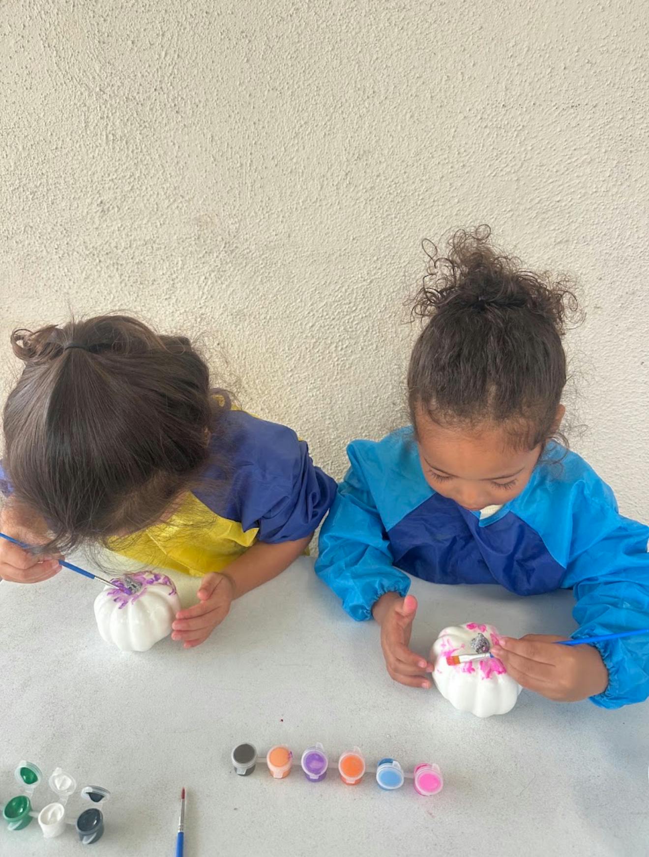 Two children painting small white pumpkins with brushes at a table