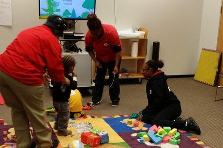Three people and a child playing with blocks on a colorful mat