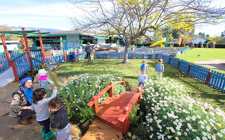 Adult and children in a garden with a small bridge and flowers