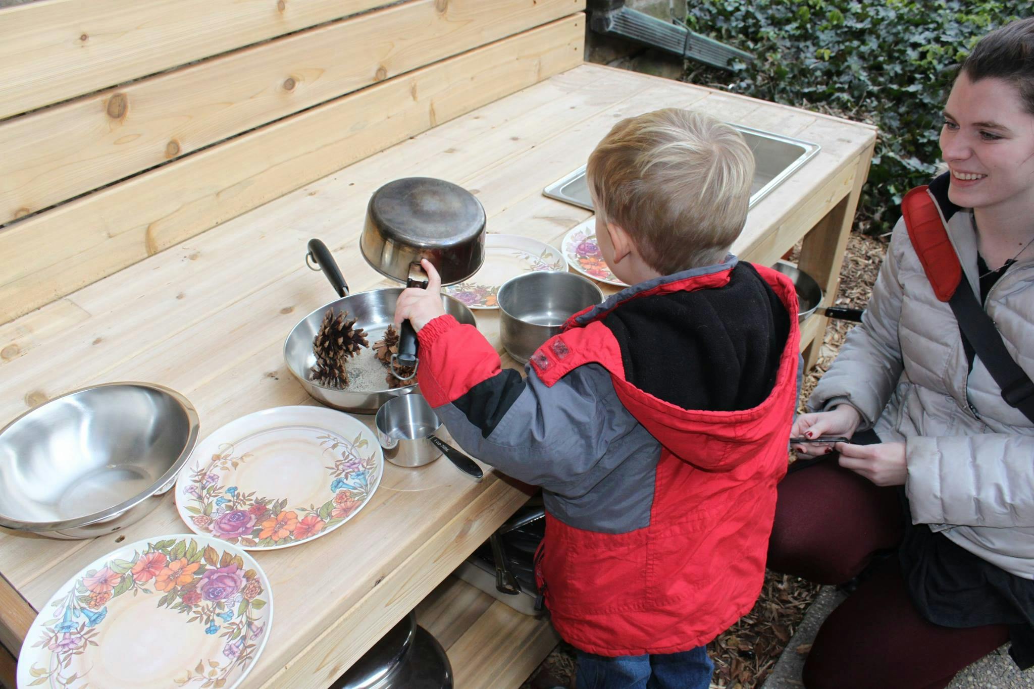 Child playing with pots and pans on a wooden surface, outdoor play kitchen