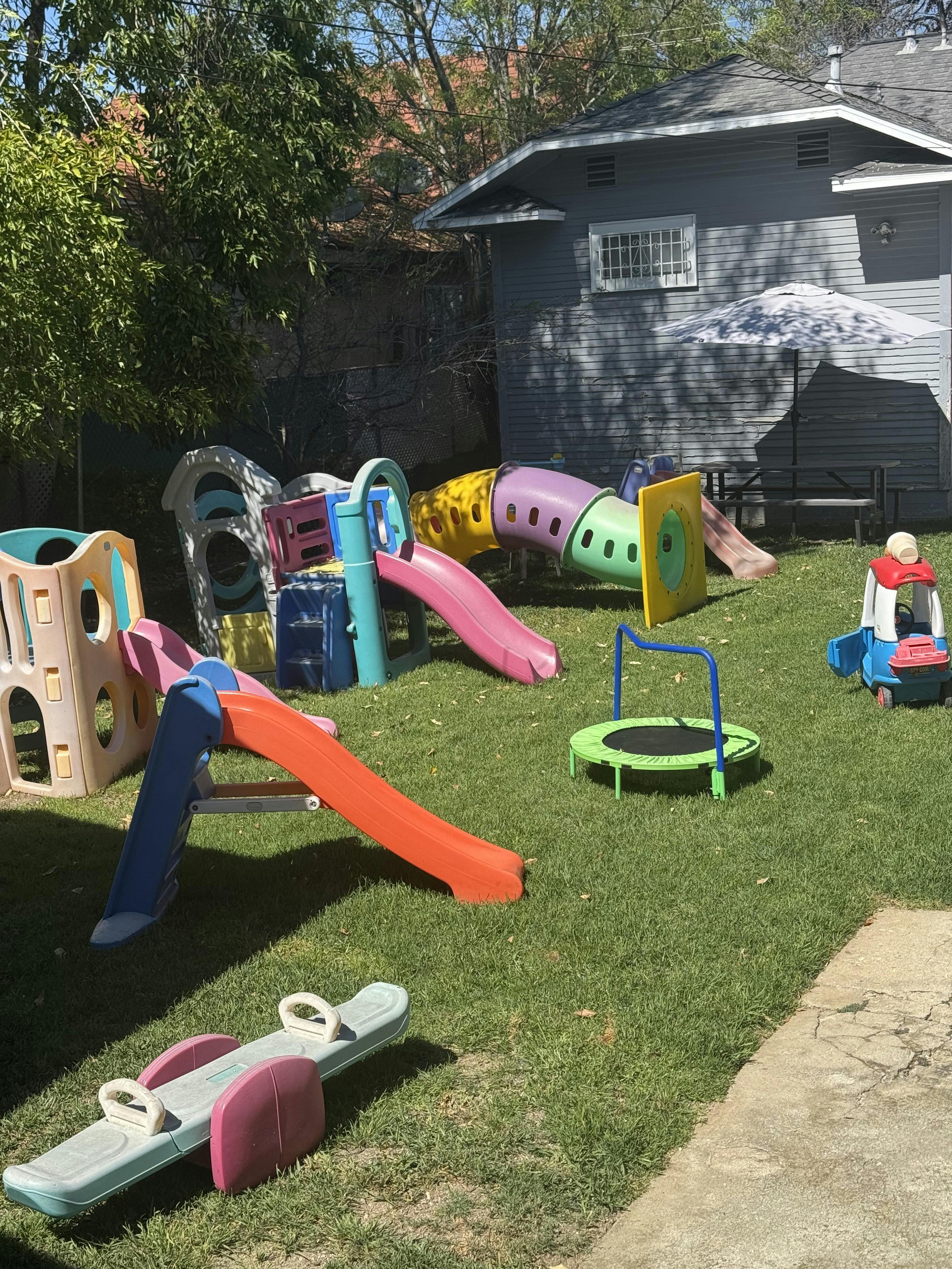 Child's playset with slides, tunnels, trampoline, and seesaw in a yard