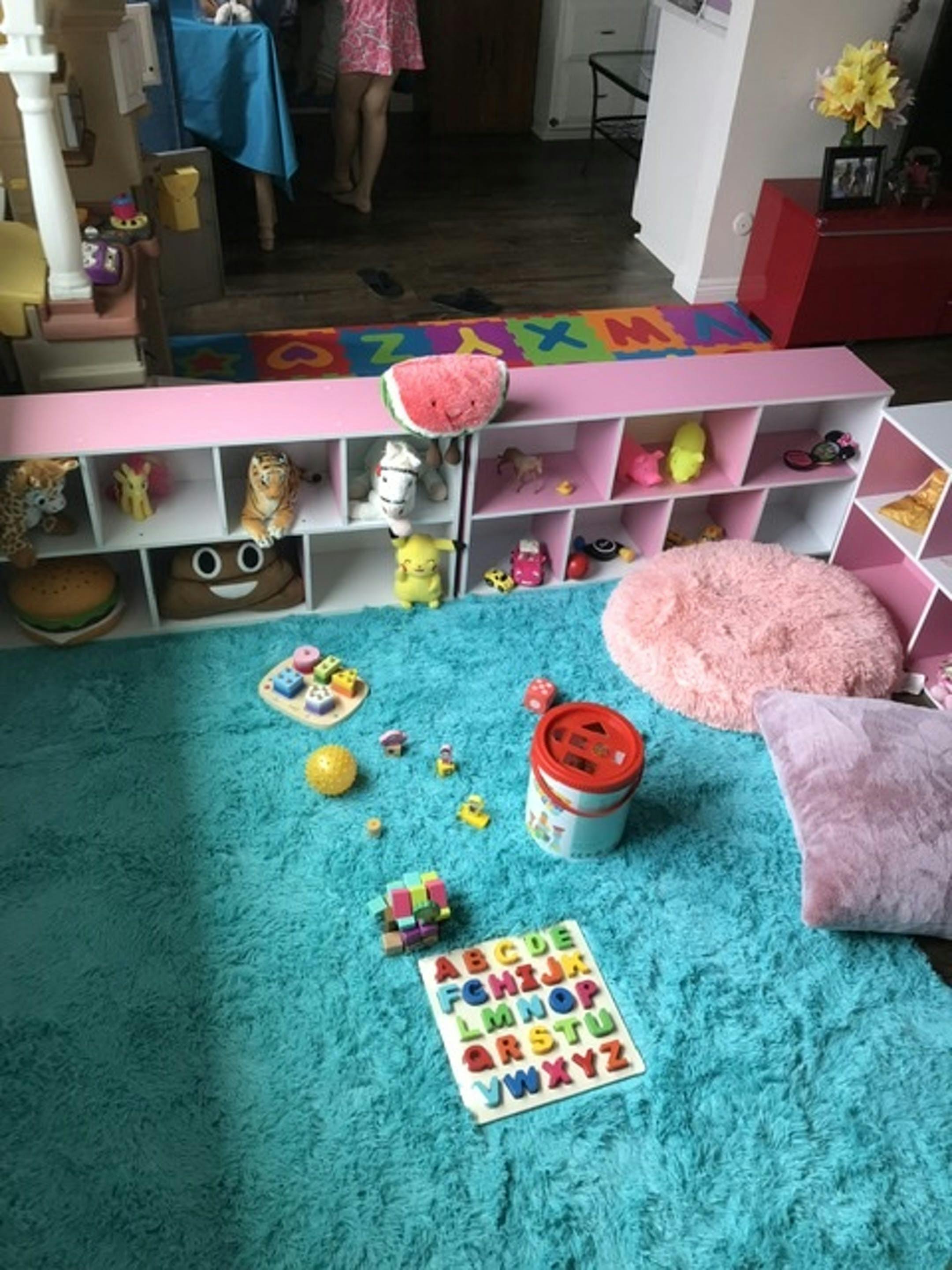 Playroom with toys on a blue rug and pink shelves