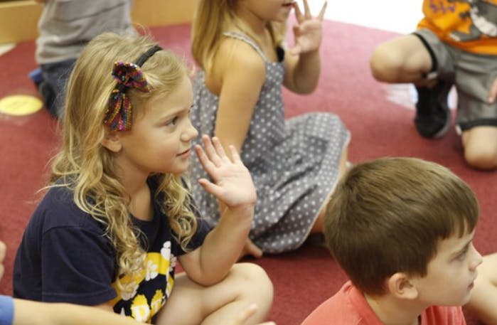 Child with long hair raising hand in a classroom