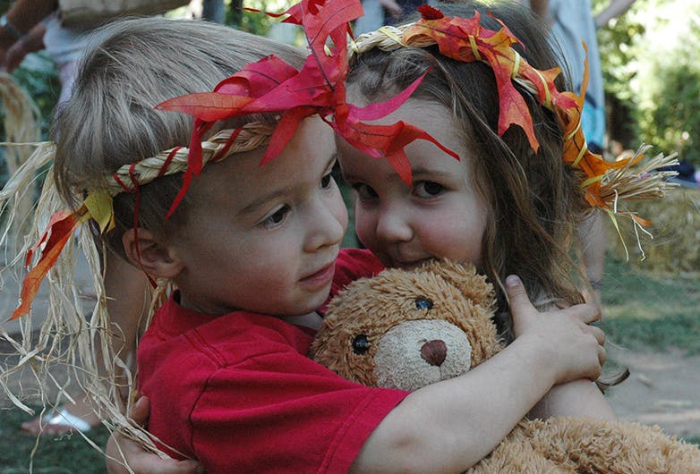 Two children wearing leaf headbands hugging a teddy bear